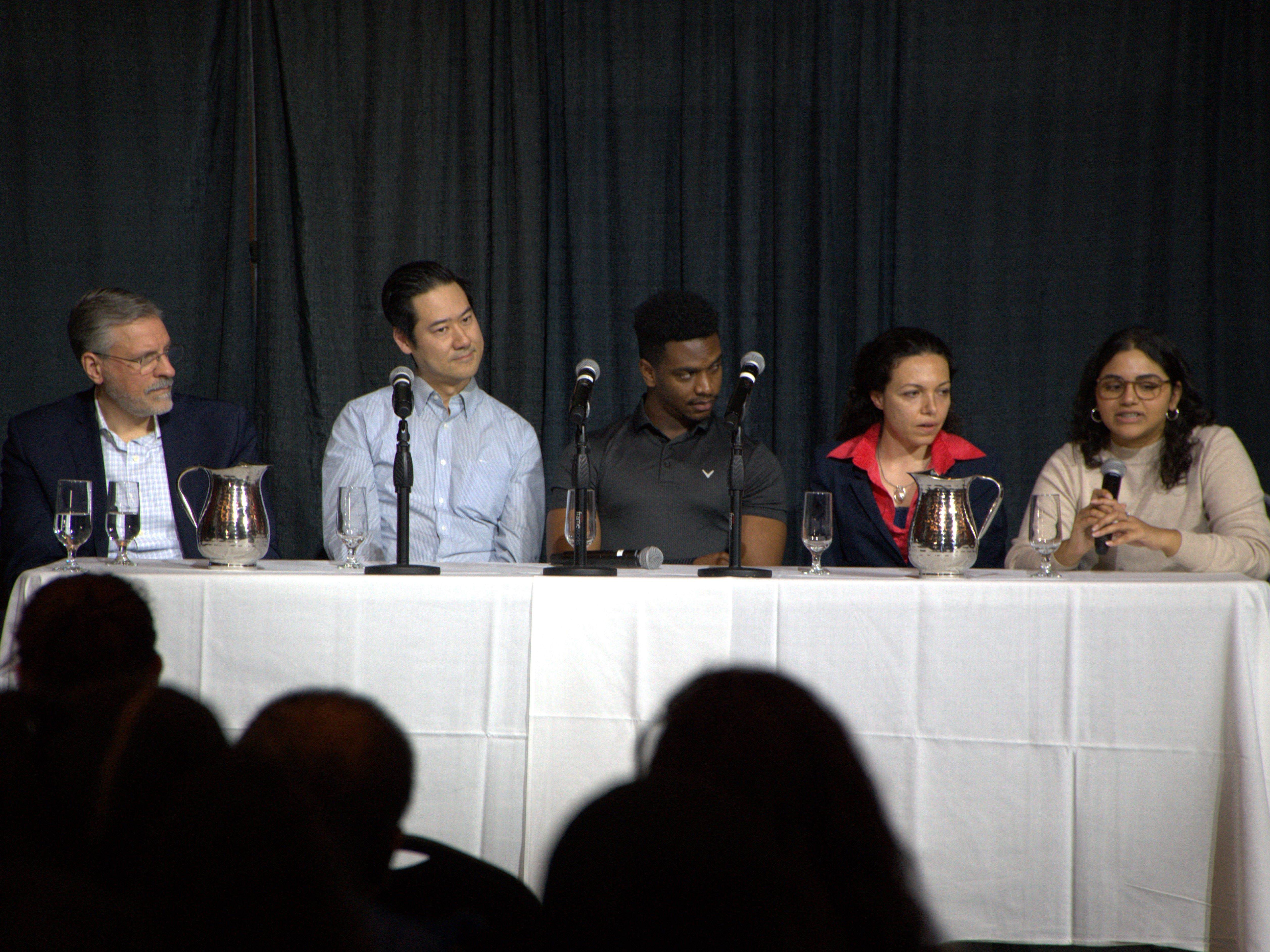 Photo of the five panelists sitting at a table on the stage